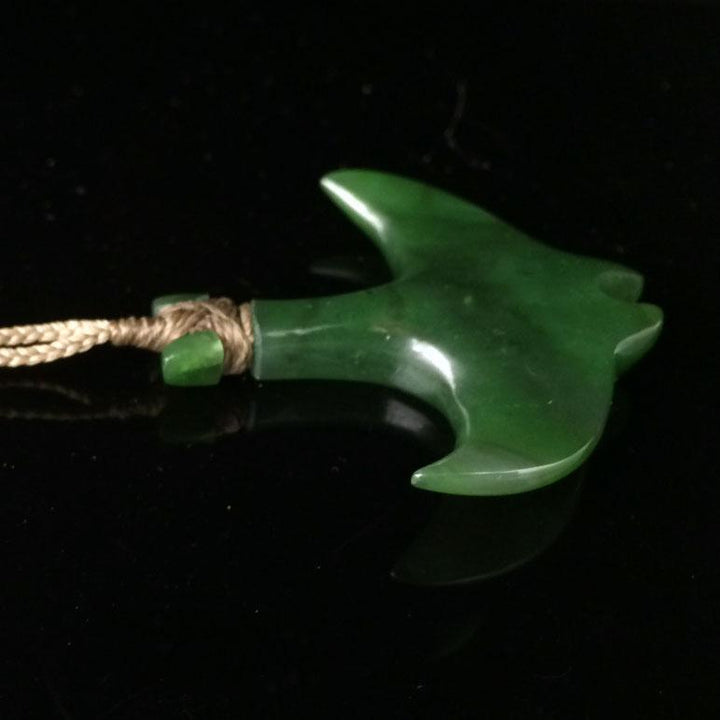 Side view of green manta ray pendant tied to a beige cord against a black background