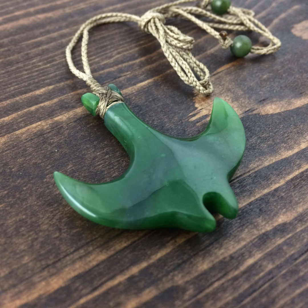 Green jade manta ray pendant with rope cord and knotted wrap on a wooden surface