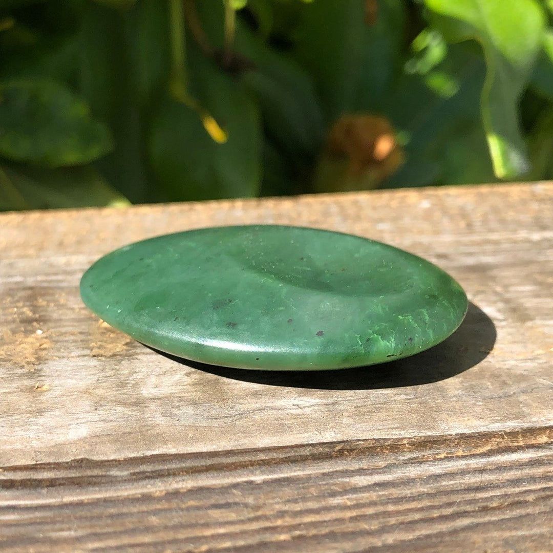 Green jade worry stone 1.75 inch satin finish resting on a weathered wooden surface outdoors.