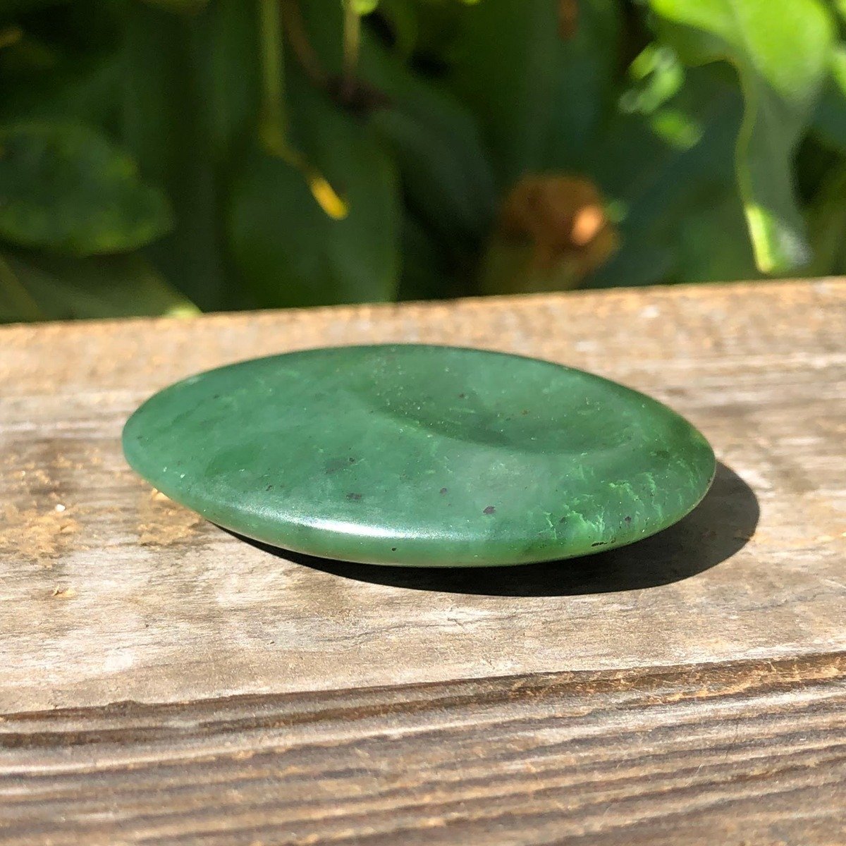 Green jade worry stone 1.75 inch satin finish resting on a weathered wooden surface outdoors.
