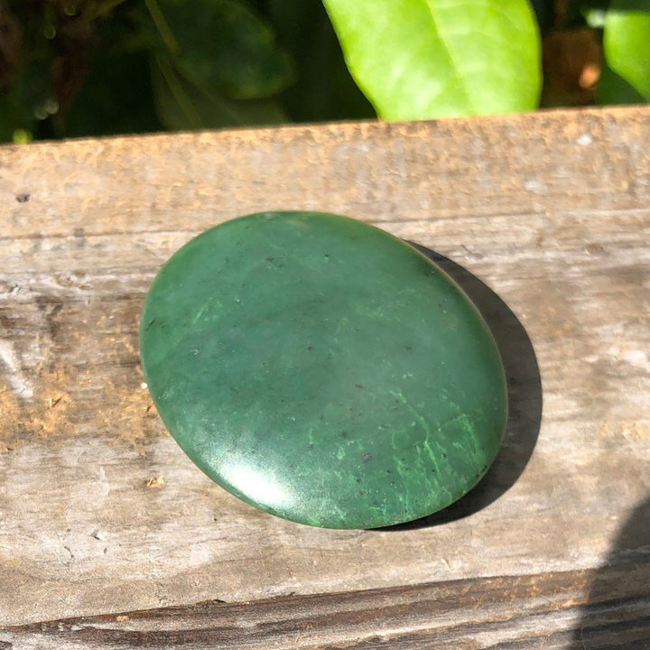 Oval green jade worry stone 1.75 inch satin finish viewed from above on a weathered wooden surface.