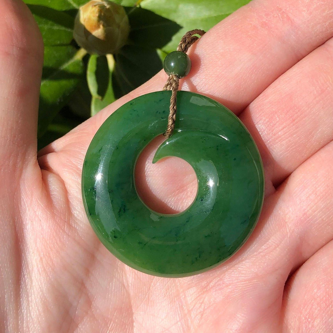 Close-up of green jade donut pendant on a brown braided cord held in a hand.