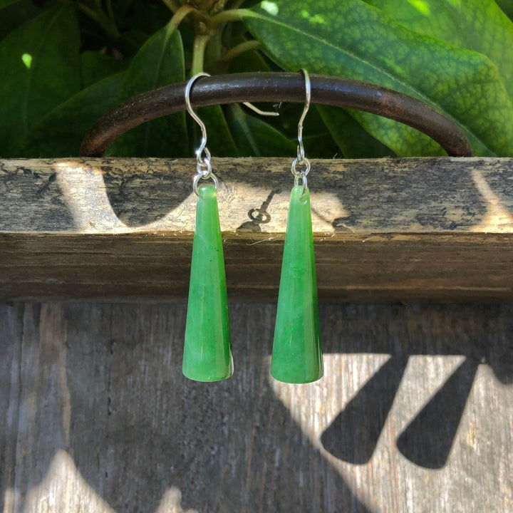 Solid jade cone earrings with silver hooks displayed on a weathered wooden surface.