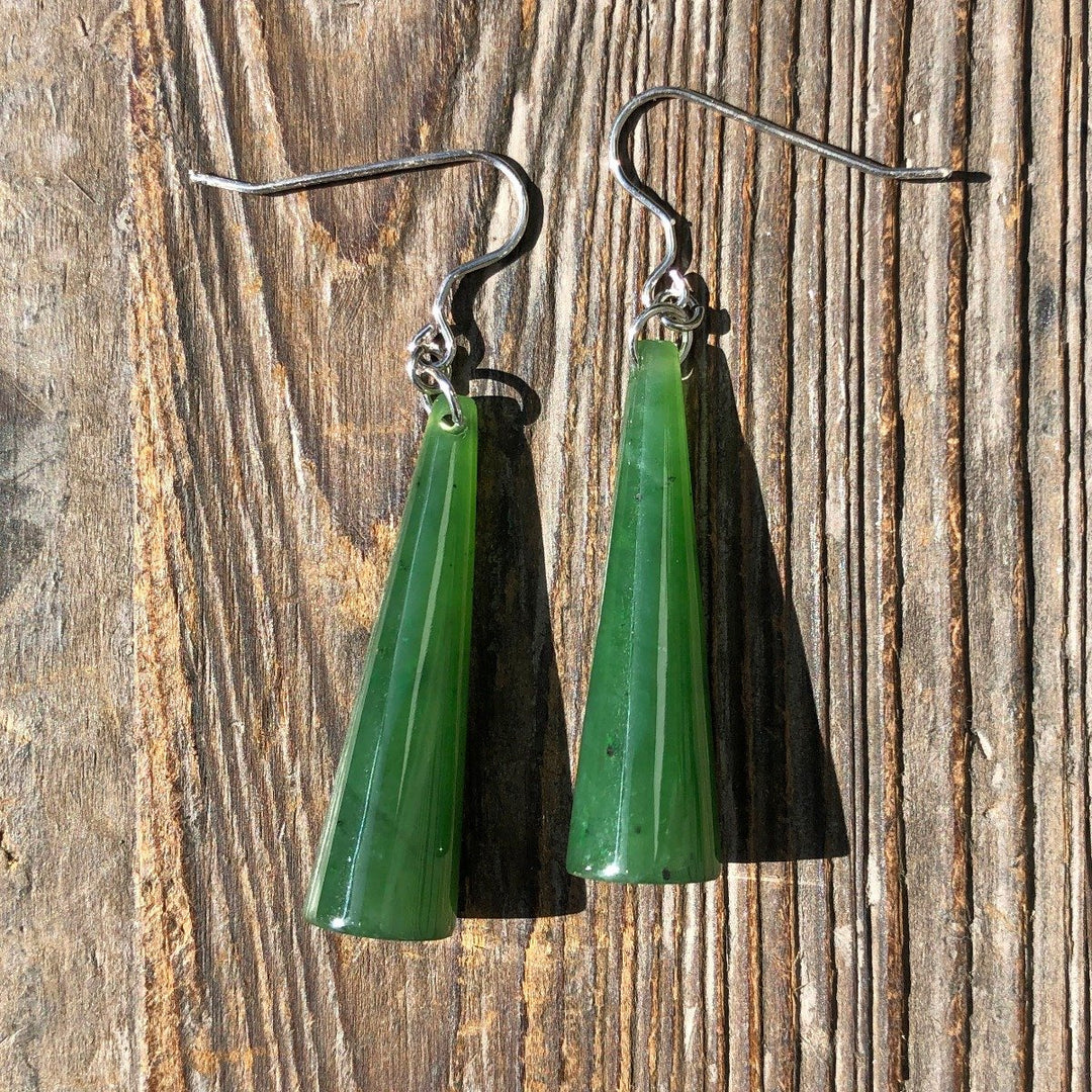 Two jade cone earrings with silver hooks laid across a textured wooden background.