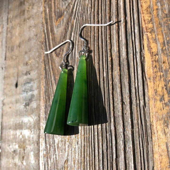 Close up of jade cone earrings on silver hooks against rough wood grain.