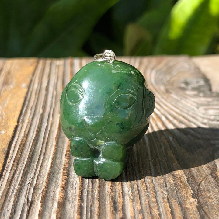 Green jade monkey charm with loop on top resting on a wooden surface.