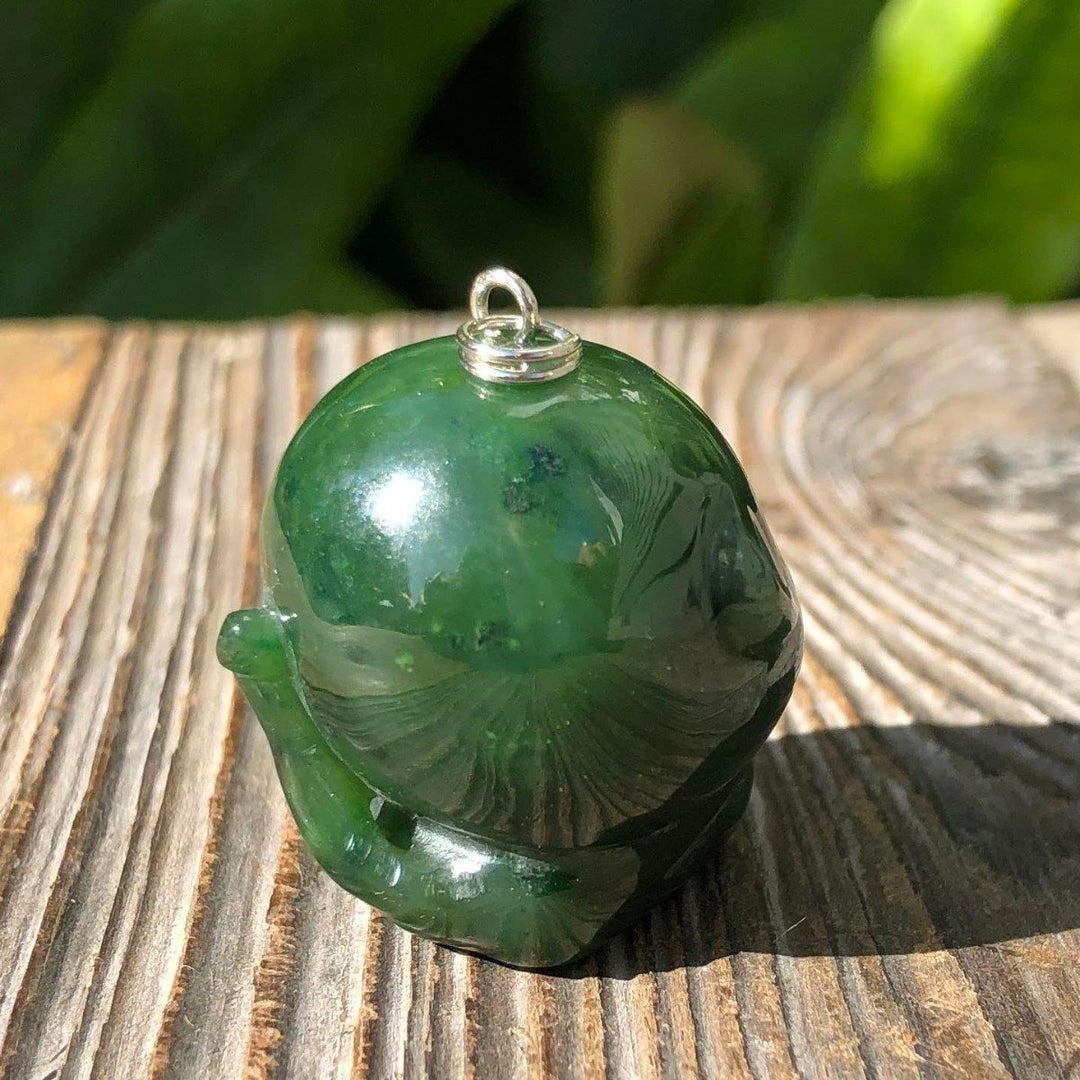 Close up of green jade monkey pendant with loop on top, resting on wood.