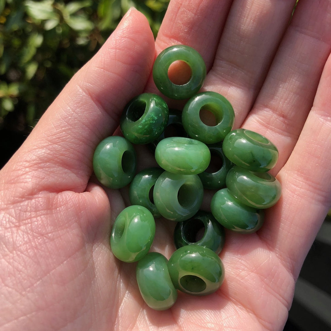 Handful of glossy green jade beads with holes held in a palm