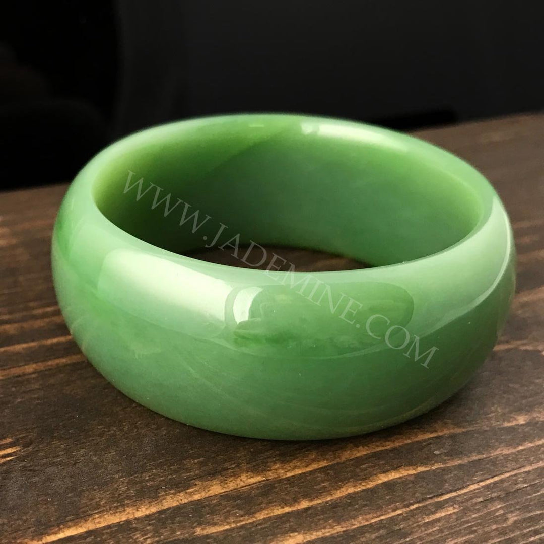AA Siberian Bangle in lighter green jade with a glossy finish on a dark wood surface