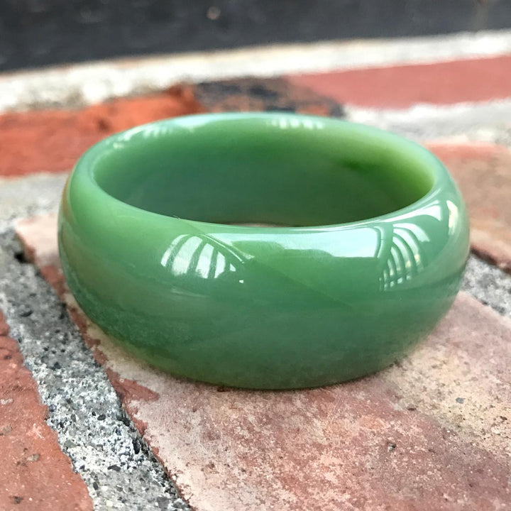 Green jade AA Siberian Bangle with a glossy finish resting on a brick surface