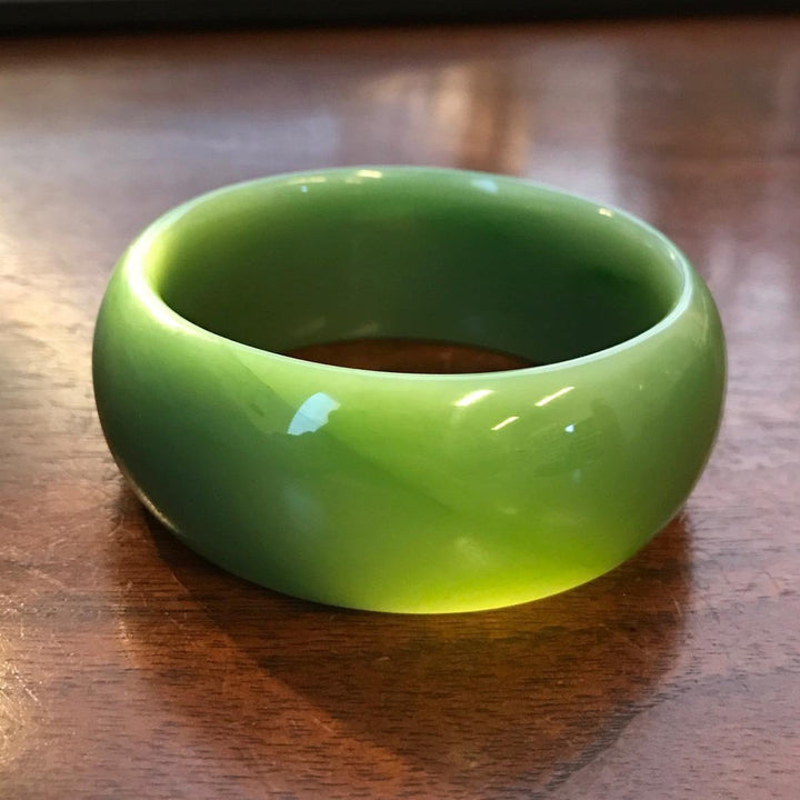 Close up of glossy green jade bangle on a wooden table showing its thick rounded shape