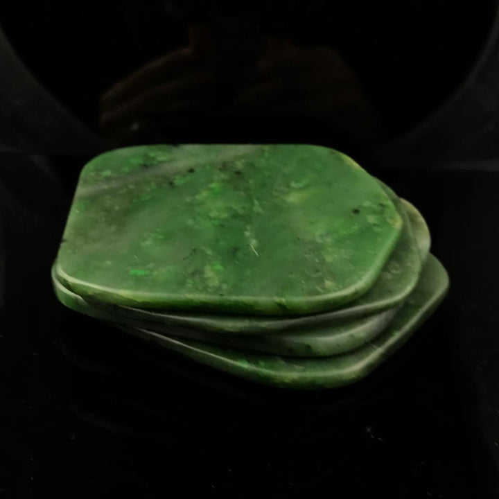 Stack of green jade coasters with rounded corners on a dark surface