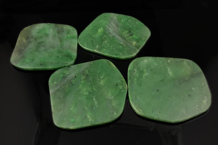Four green jade coasters with rounded edges arranged on a dark surface