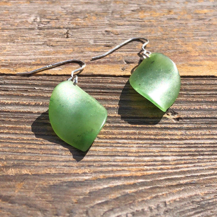 Green leaf shaped earrings with silver hooks lying on a rustic wooden surface