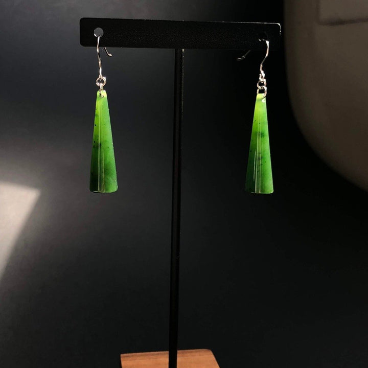 Green jade cone earrings with silver hooks displayed on a black stand
