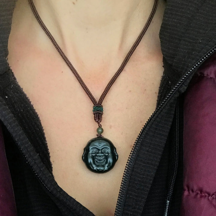Happy Buddha head pendant on a dark brown braided necklace with a green knot and bead, worn at the chest.