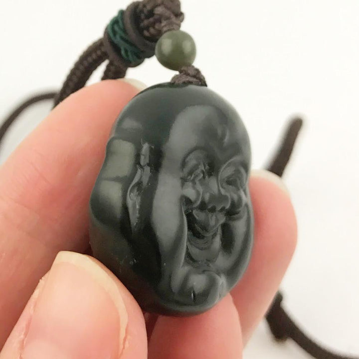 Side view of the dark green Buddha head pendant on a brown cord with a green bead, held between fingers