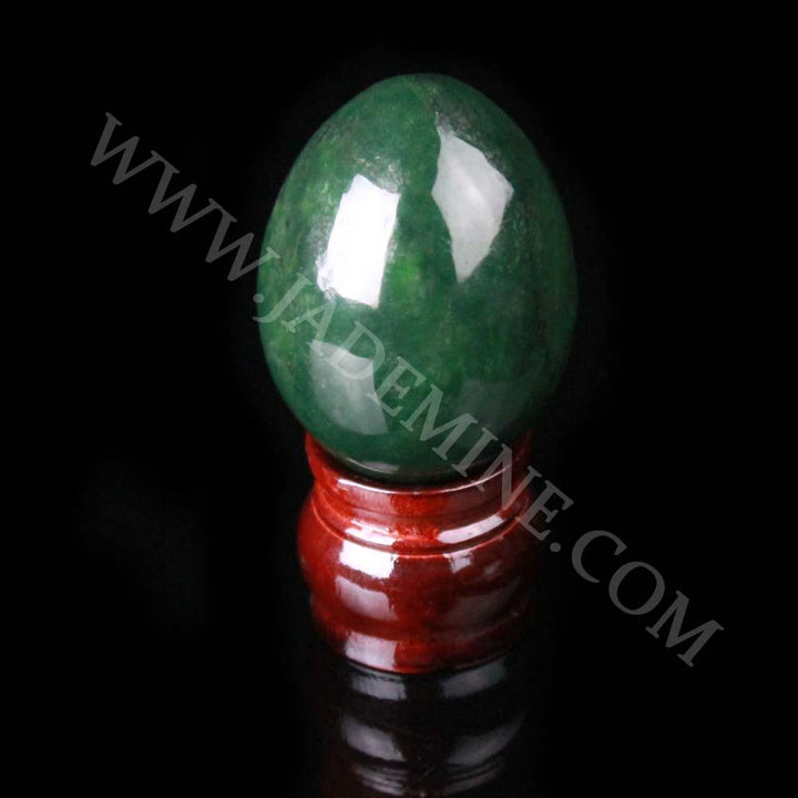 Polished green gemstone egg perched on a glossy red stand against a black background.