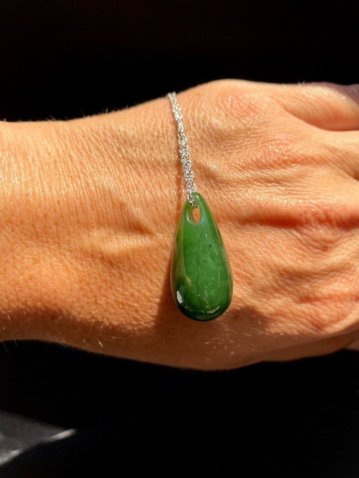 Jade teardrop pendant on a silver chain shown resting on a hand