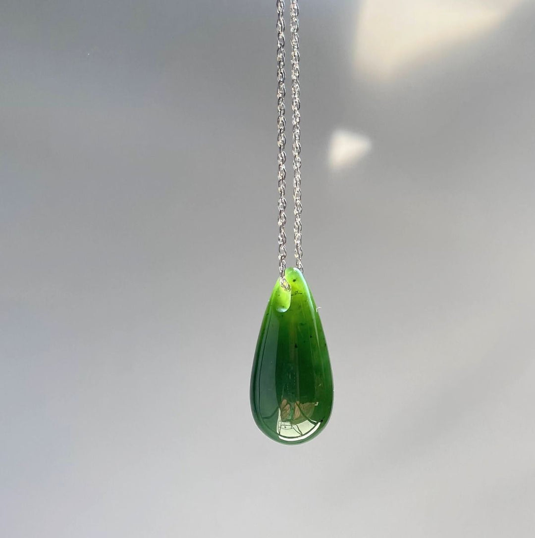 Jade teardrop pendant on a silver chain hanging against a pale gray background