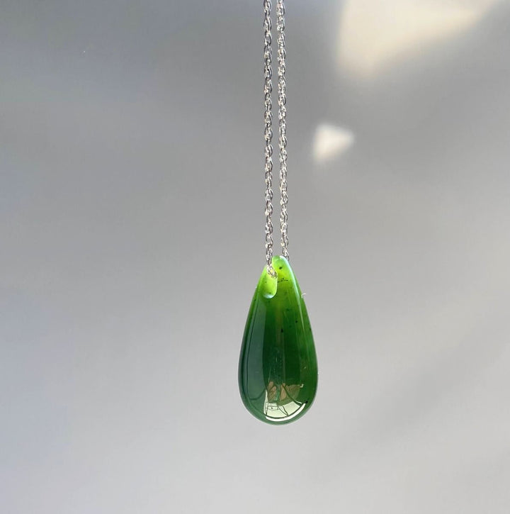 Jade teardrop pendant on a silver chain hanging against a pale gray background