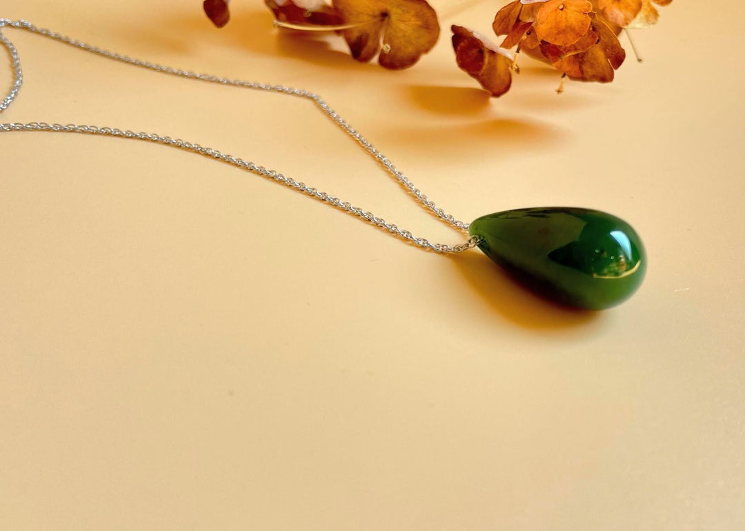 Green jade teardrop pendant on a silver chain against a pale yellow background