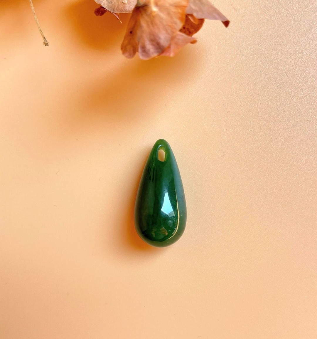 Green jade teardrop pendant with a hole at the top on a peach background