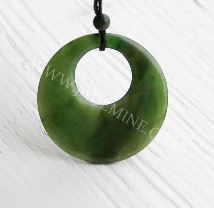 Close-up of circular green jade pendant with central hole on black cord