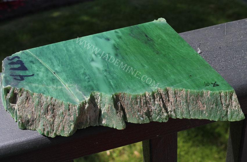 AA Siberian Rough jade slab showing a smooth green surface and jagged brown base on a deck railing.