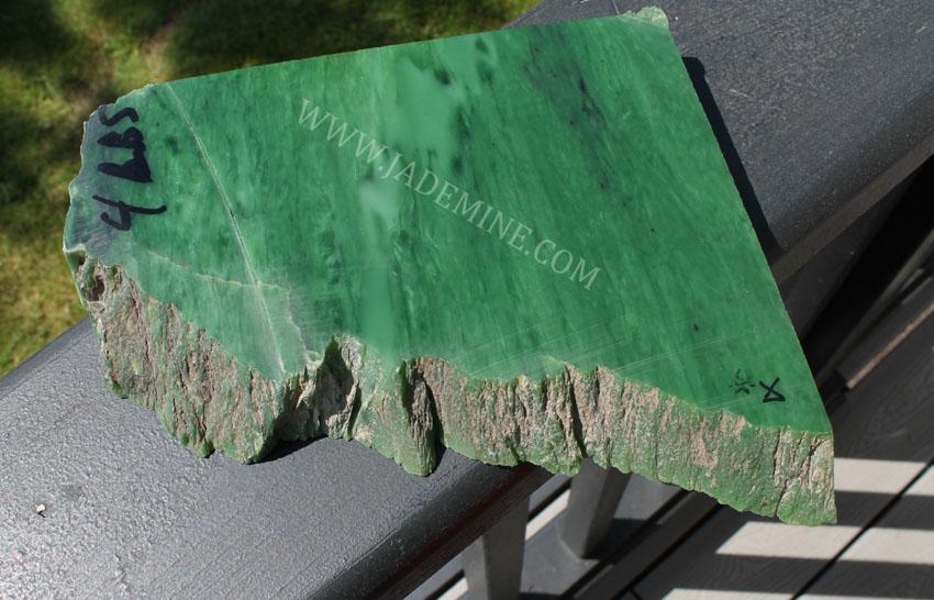 AA Siberian Rough jade chunk with bright polished green face and rough rocky bottom on a railing.