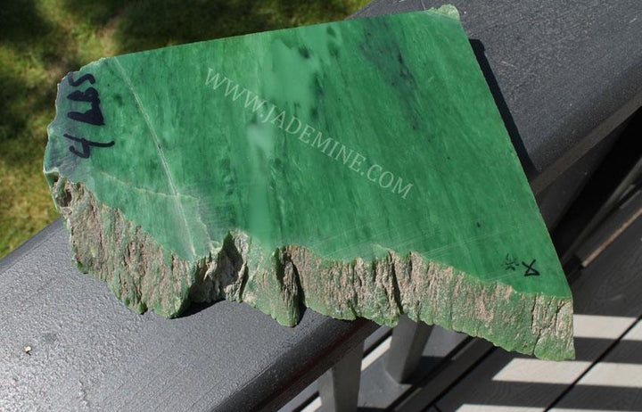 AA Siberian Rough jade chunk with bright polished green face and rough rocky bottom on a railing.
