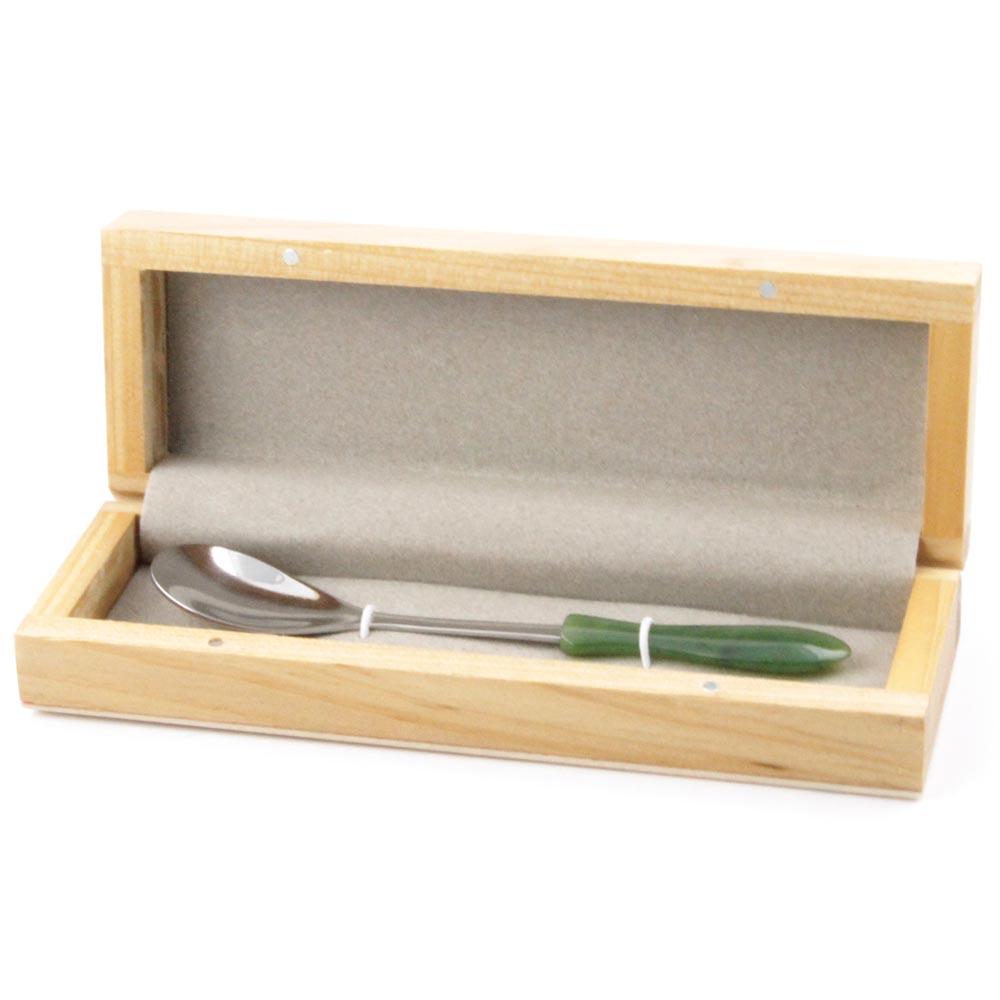 Jade sugar spoon resting in a light wooden display box with grey lining.