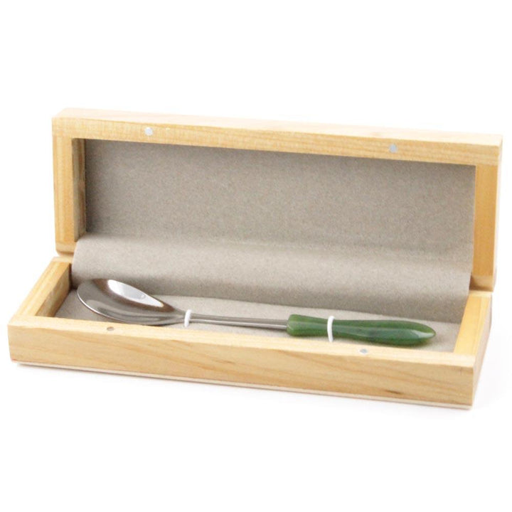 Jade sugar spoon resting in a light wooden display box with grey lining.