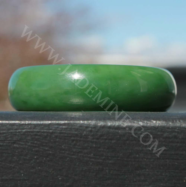 AA Siberian Jade Bangle 58x18mm polished green on a dark wood background