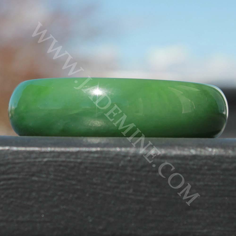 AA Siberian Jade Bangle 58x18mm in vivid green resting on dark wood surface