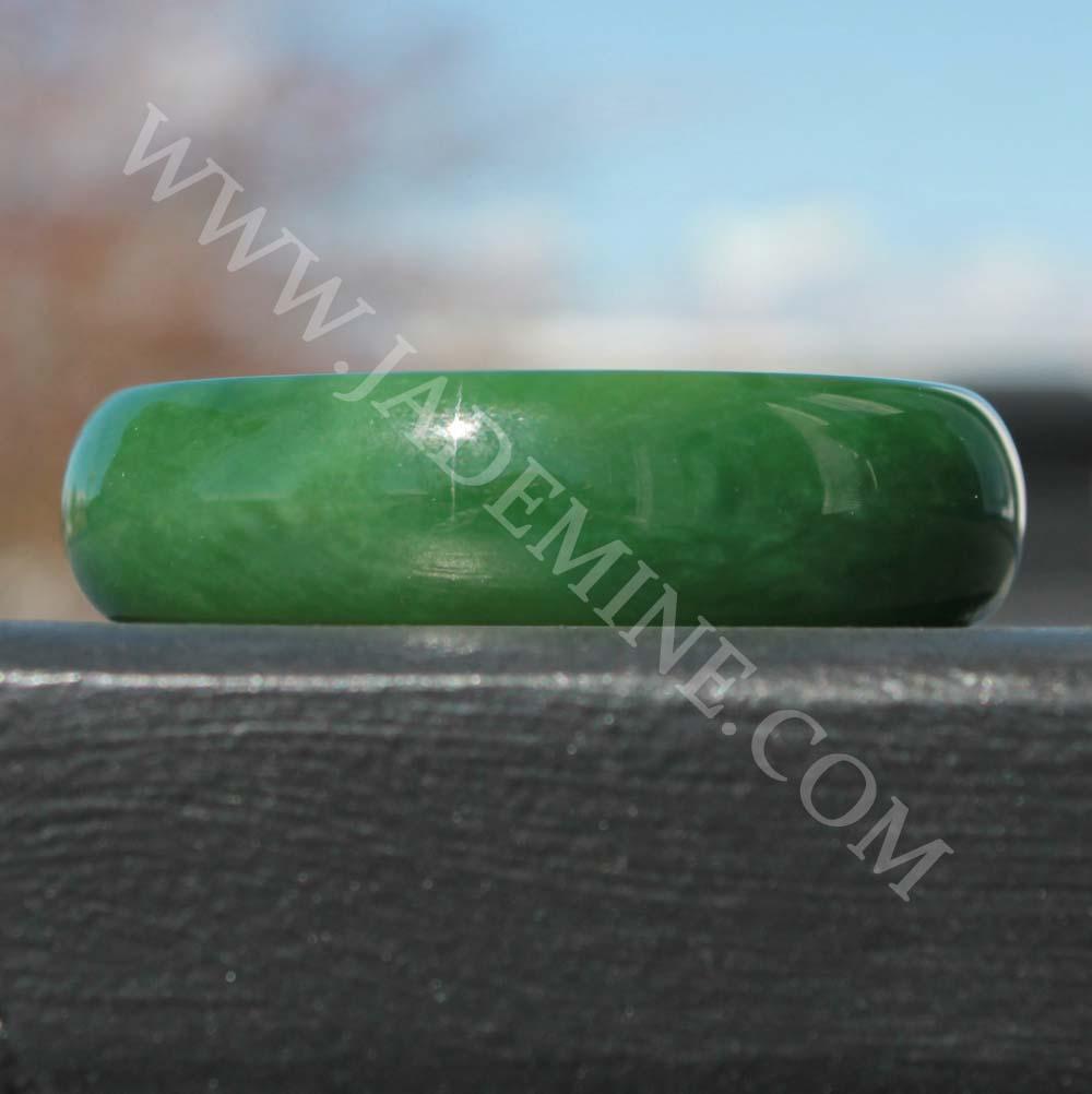 Green jade bangle resting on a dark wooden ledge in outdoor light.