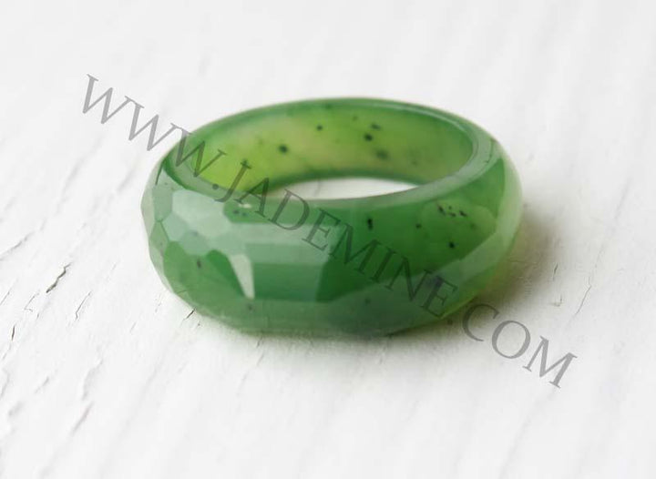 Green faceted band ring with a wide angular surface on a white background