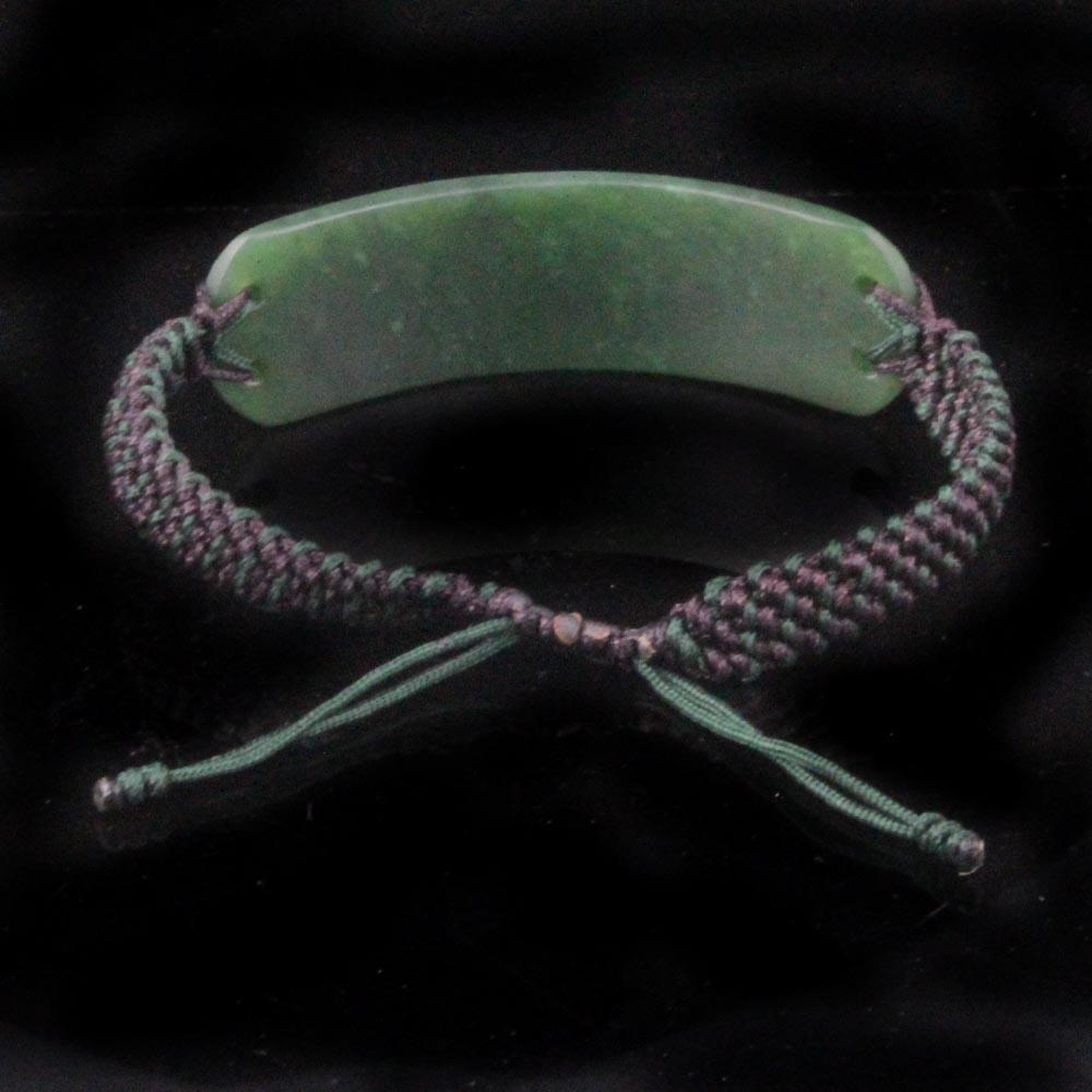 Green jade centerpiece with a purple and green braided cord bracelet and knotted ends against black background.