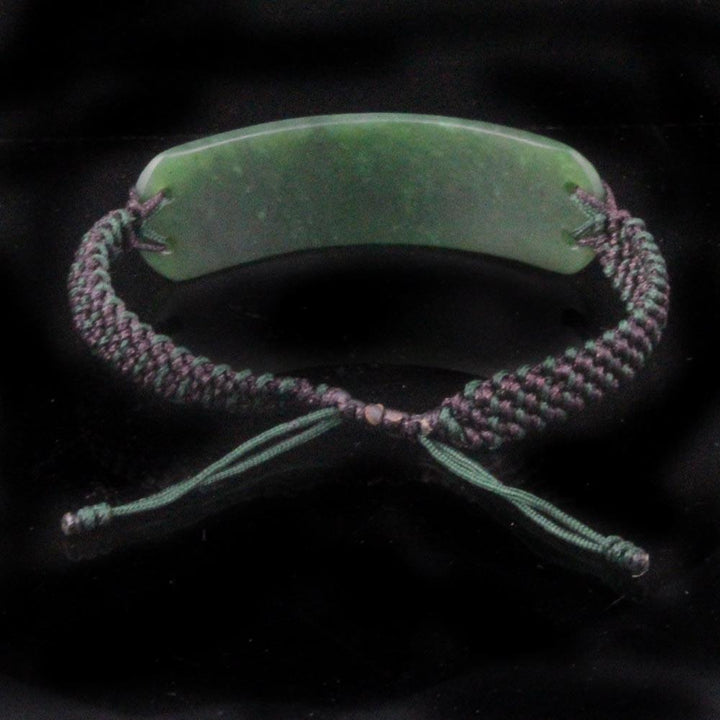 Green jade centerpiece with a purple and green braided cord bracelet and knotted ends against black background.