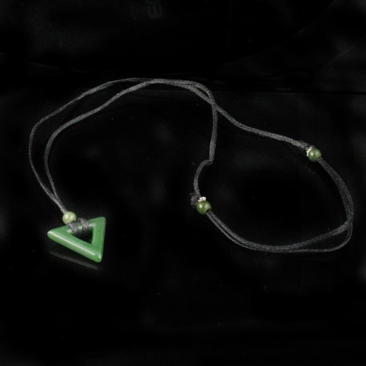 Front view of jade triangle pendant on black cord with a green bead against a dark background.