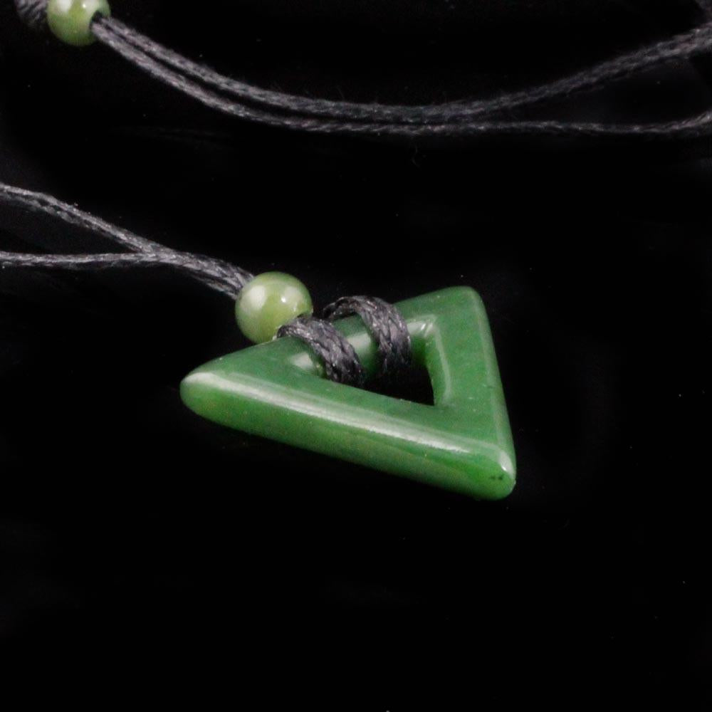 Close up of jade triangle pendant threaded by a dark cord with a wrapped knot and small green bead.