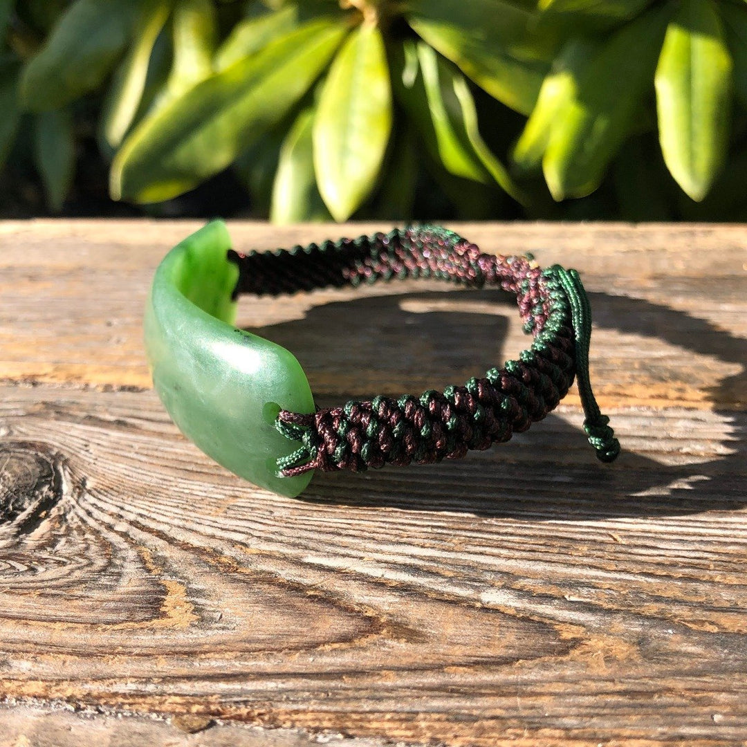 Green jade centerpiece bracelet with maroon and green braided cord resting on a wooden surface.