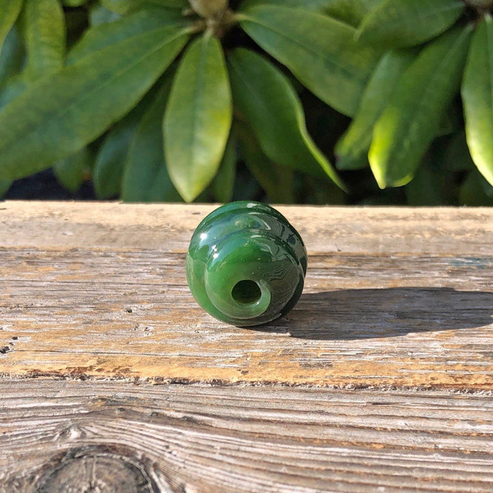 Rich green carved jade bead with central hole and swirling patterns on wood
