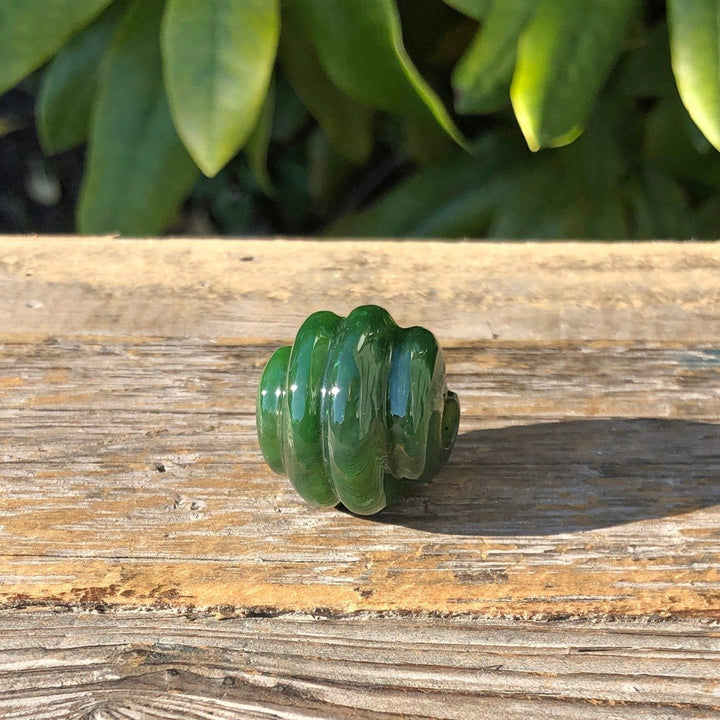 Rich green carved jade bead with spiral grooves and central hole on wooden surface