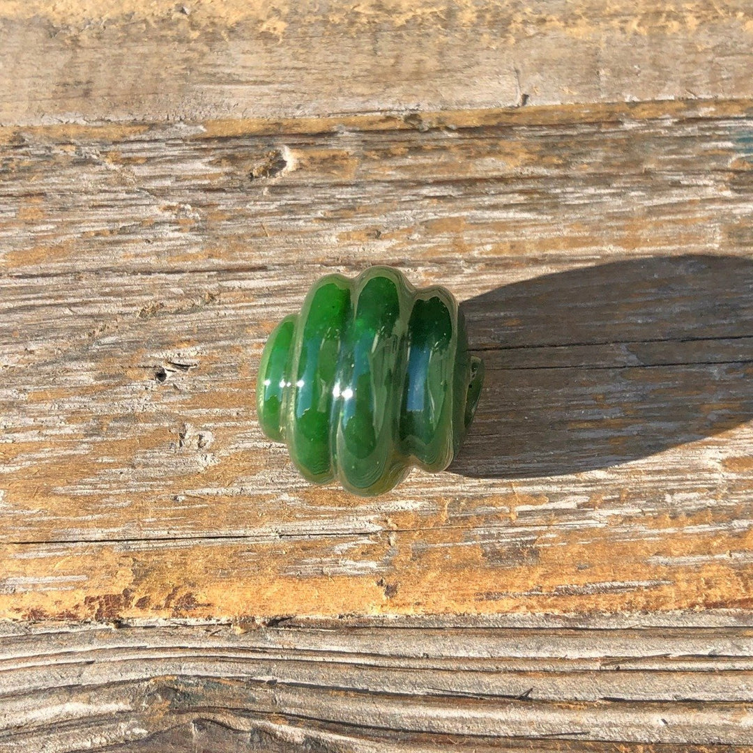 Rich green carved jade bead with stacked rounded rings and central hole on weathered wood