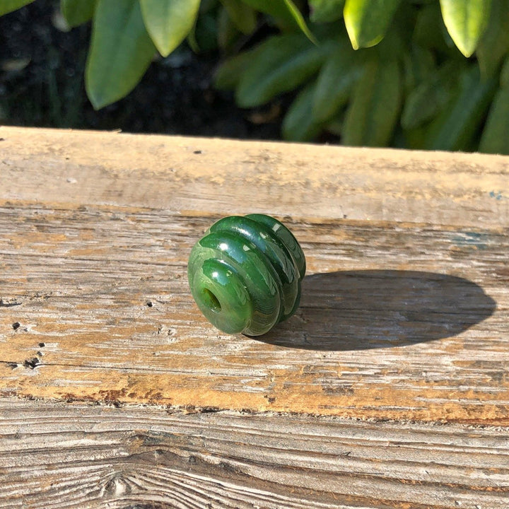 Close up of a rich green carved jade bead with spiral rings and a central hole on wood