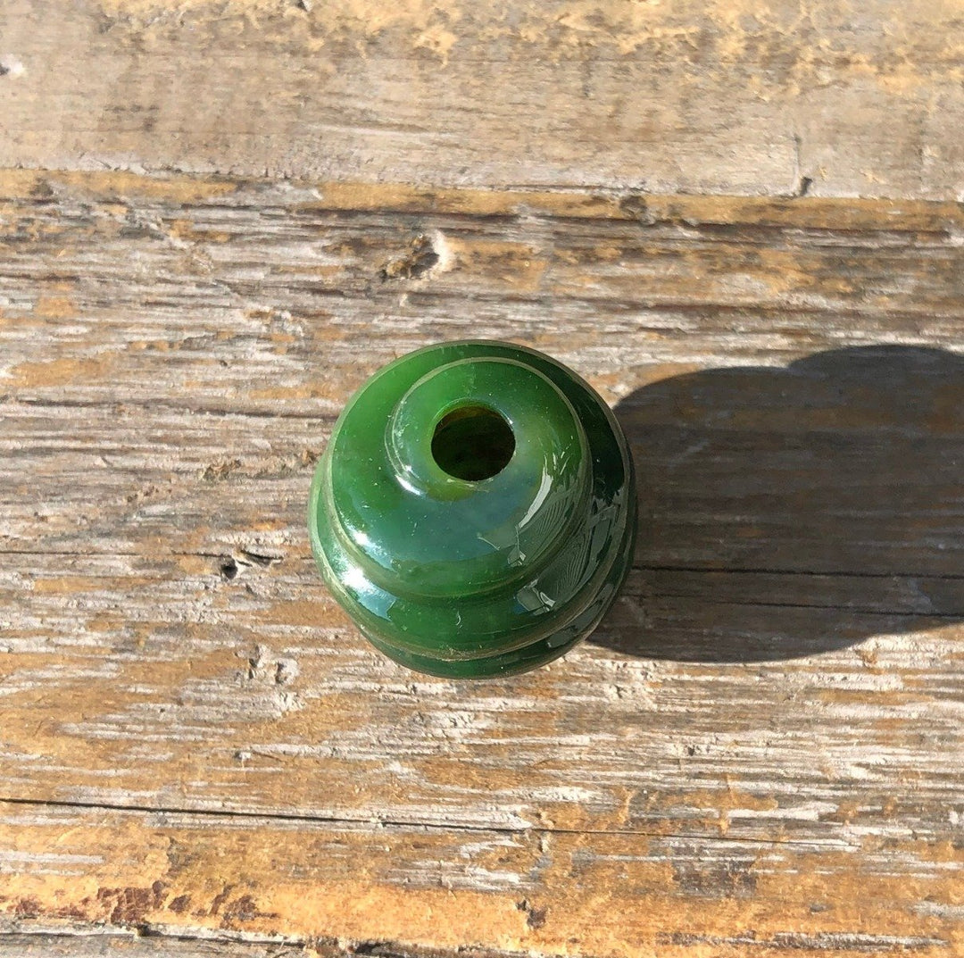 Rich green carved jade bead with a central hole on a rustic wooden surface