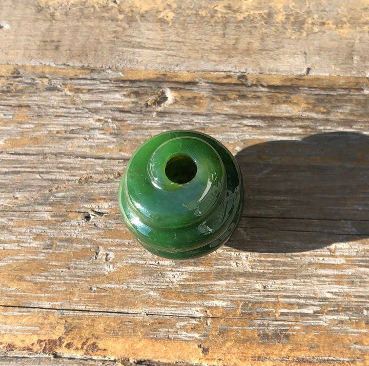 Rich green carved jade bead with a central hole on a rustic wooden surface