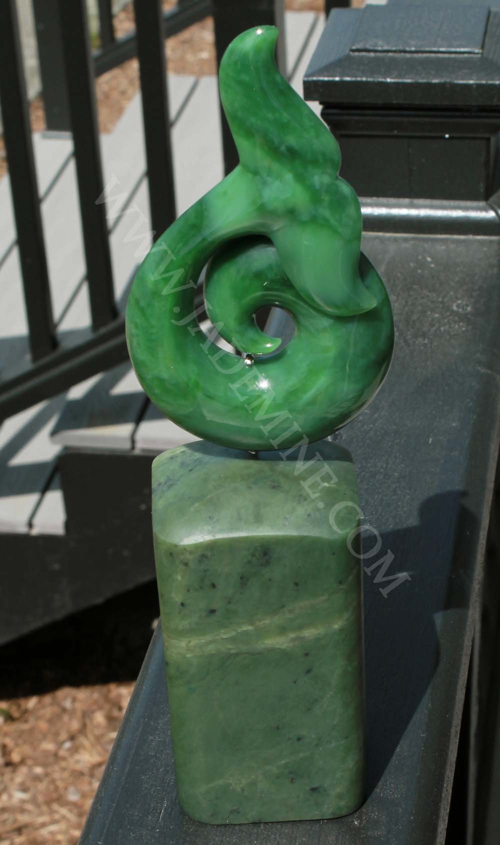 Glossy green jade whale tail sculpture with a curling tail perched on a rectangular jade base.