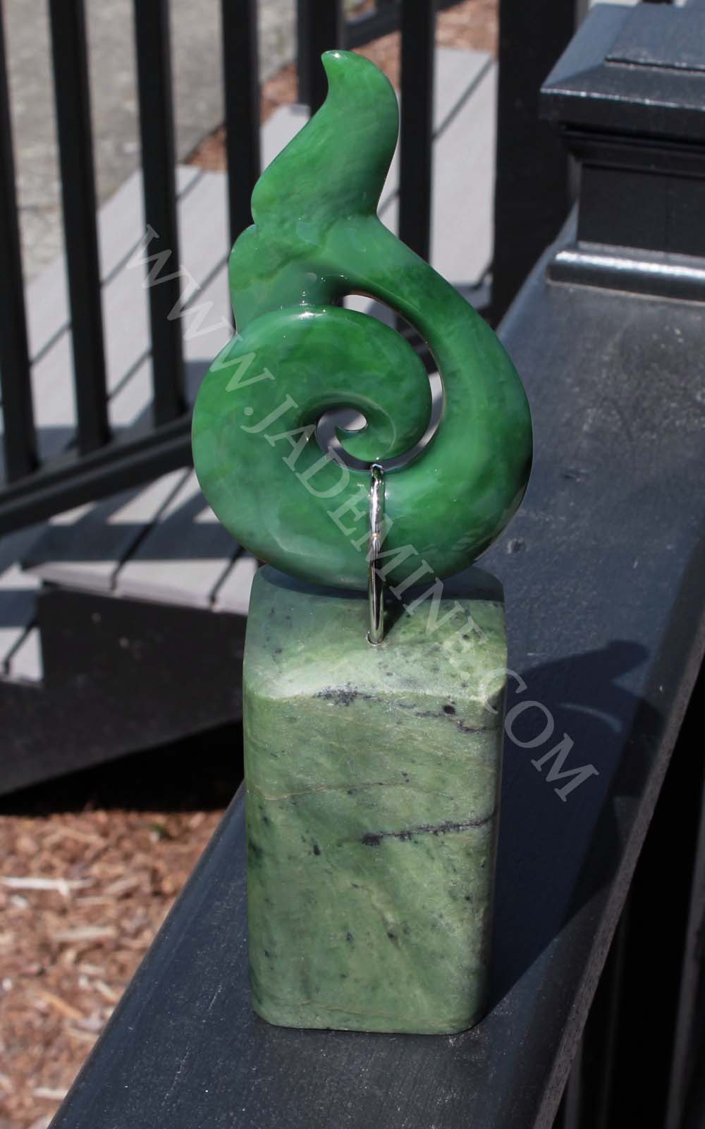 Green jade whale tail sculpture on a rectangular jade base with a metal ring.